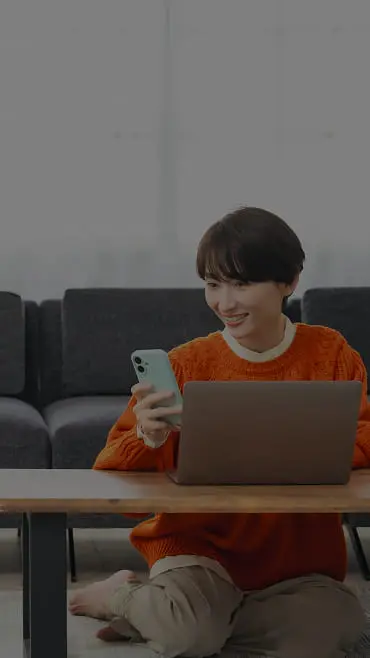笑顔でスマホとパソコンを操作する女性の様子